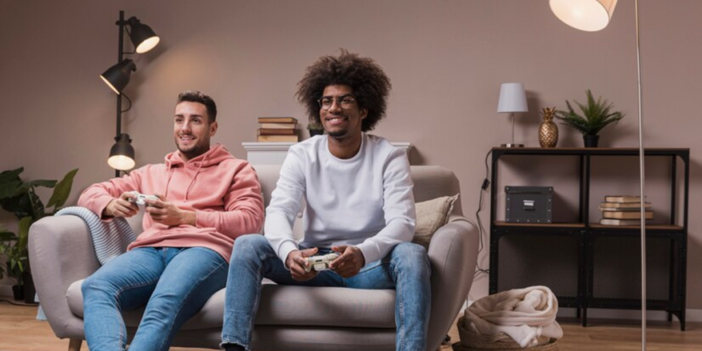 Two friends enjoy playing video games at home after sorting out their Air Conditioner bill.